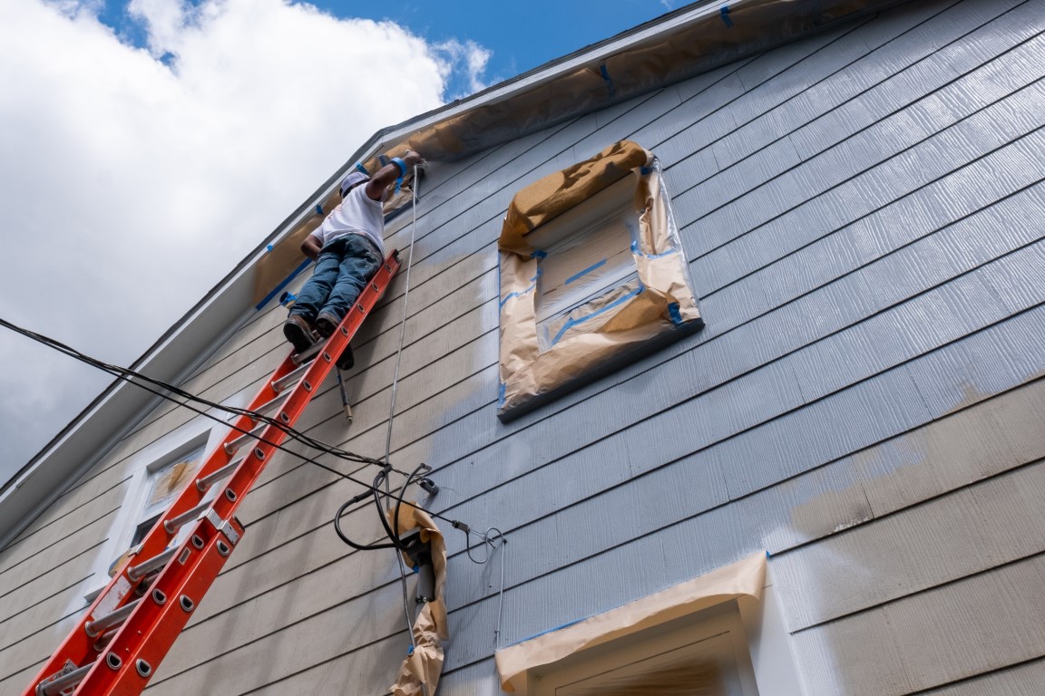 Painter on a ladder spraying paint on the exterior of a house